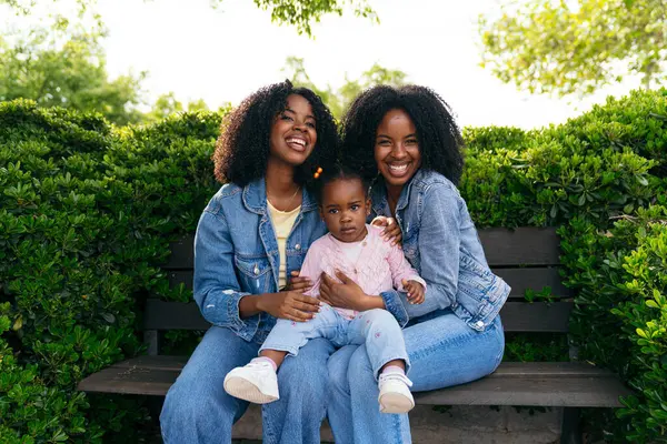 Afrikalı ikiz kardeşler, yemyeşil yemliklerle çevrili bir bankta oturup yeğenleriyle güzel vakit geçiriyorlar.