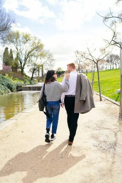 Genç çift parkta sakin bir gölün kenarında el ele geziniyor güneşli bir günün sıcaklığında güneşleniyor ve birlikte geçirdikleri zamanı kutluyorlar.