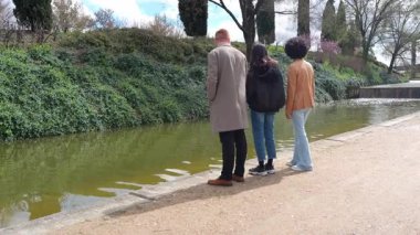 Bir grup arkadaş parkta kanalın yanında fotoğraf için poz veriyor, kameraya bakmaktan kameraya bakmaya geçiyor, yavaş çekim.