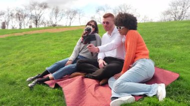 Sunny Park 'ta piknik battaniyesinde otururken podcast bölümü kaydeden genç içerik yaratıcıları, mikrofon ve mobil cihazlarla ses ve video içeriği üzerinde işbirliği yapıyorlar.