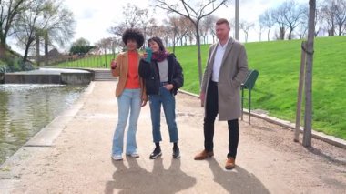 Üç meslektaş, iki kadın ve bir erkek, parkta yürürken ve konuşurken kahve molası veriyorlar.