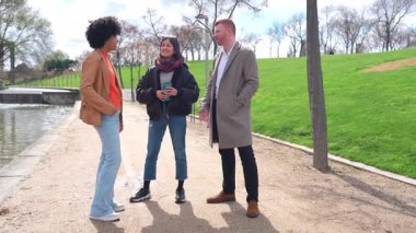 Üç arkadaş güneşli bir günde parkta bir kanalın kenarında sohbet etmekten zevk alırlar, ağır çekimde yakalanırlar.