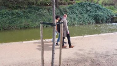 Öğrenci grubu, güneşli bir bahar gününde yemyeşil şehir parkında nehir kıyısında yürürken, kaygısız dostluğu ve gevşek bağlantıyı yavaş çekim görüntüleriyle yakalıyorlar.