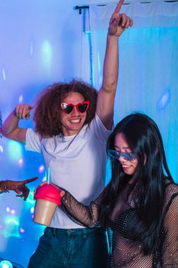 Mutlu çoklu etnik arkadaşlarla kutlamak, canlı bir partide canlı mavi disko ışıkları altında dans etmek ve renkli kokteyller içmek.