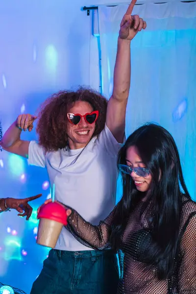 Mutlu çoklu etnik arkadaşlarla kutlamak, canlı bir partide canlı mavi disko ışıkları altında dans etmek ve renkli kokteyller içmek.