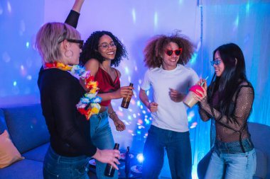 Neşeli, etnik çeşitliliğe sahip bir grup arkadaş disko ışıklarıyla canlı bir ev partisinde içki içip dans ediyorlar.