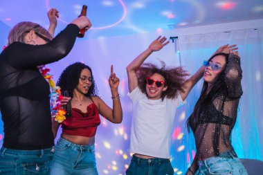 Bir grup neşeli çoklu etnik arkadaş ev partisinde eğleniyor, dans ediyor ve renkli disko ışıkları altında eğleniyorlar.