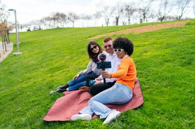 Parkta güneşli bir günün tadını çıkaran üç arkadaş, akıllı telefon ve mikrofonla canlı bir video bloğu çekiyorlar, kahkaha ve yaratıcılığı paylaşıyorlar.
