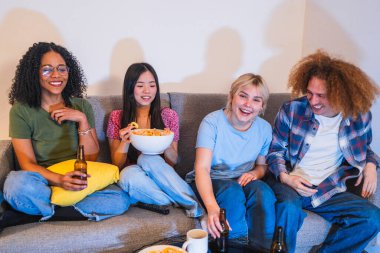 Dört genç çok ırklı arkadaş televizyon izlerken gülüyor, abur cubur yiyor ve gri bir kanepede bira içiyor.