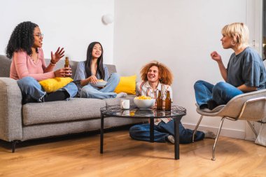 Neşeli çoklu etnik arkadaşlar rahat bir ev partisinde eğleniyor, bira içiyor, cips yiyor ve sohbet ediyor ve birlikte gülüyorlar.