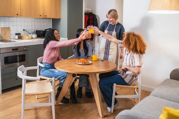 Dört genç, etnik çeşitliliğe sahip bayan arkadaş evde birlikte kahvaltı ederken portakal suyuyla kadeh kaldırıyorlar.