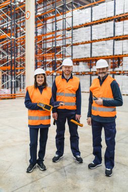 Güvenlik yelekleri ve miğfer takan lojistik işçileri taşınabilir barkod tarayıcıları ve radyo vericileri taşıyorlar, büyük bir dağıtım deposunda envanter ve işlemleri yönetiyorlar.