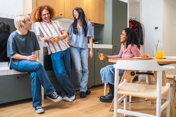 Mutlu çoklu etnik arkadaşlar kahvaltı, meyve suyu ve kahkahaları modern bir mutfakta paylaşıyor ve birlikte vakit geçiriyorlar.