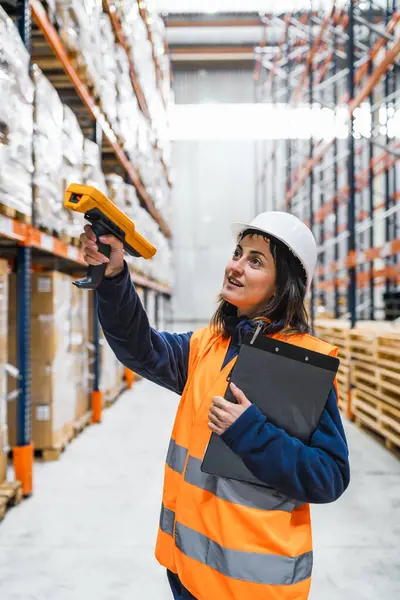 Depo çalışanı barkod okuyucusuyla yüksek rafları tarıyor, büyük bir dağıtım merkezinde envanter ve lojistiği yönetiyor.