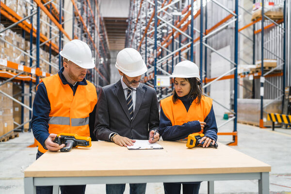 Manager signing documents with warehouse workers holding barcode scanners in a logistics center