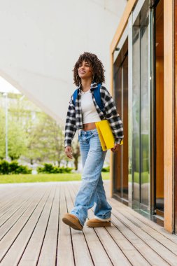 Laptopuyla çalışan Latin kökenli genç bir öğrenci ve üniversite merdivenlerinde otururken akıllı telefonla konuşuyor.