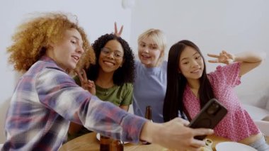 Çoklu etnik arkadaş grubu, pizza ve birayla selfie çekerken neşeli anları paylaşıyor, gerçek bağlantıları ve günlük toplantılar sırasında neşeli sosyal etkileşimleri sergiliyor.