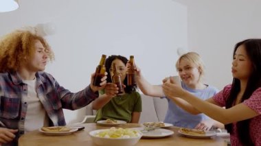 Çok ırklı arkadaşlar bir ev partisinde içki ve atıştırmalıkların tadını çıkarıyor, yavaş çekimde kadeh kaldırıyor ve gülüyorlar.