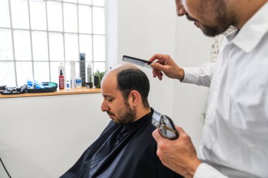 Kuaför, özel bir kuaför kliniğinde saç nakli işlemi için müşterinin saçını ustalıkla tarayıp hazırlıyor.