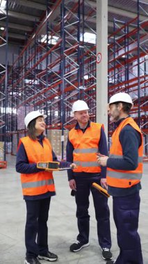 Depo çalışanları lojistik ve envanter yönetimini tartışıyor, bir dağıtım merkezinde etkili bir şekilde gülümsüyor ve işbirliği yapıyorlar.