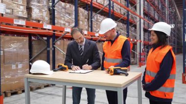 İşletme müdürü bir sözleşme imzaladı ve depo çalışanlarıyla el sıkıştı. Başarılı bir anlaşma imzalandı.