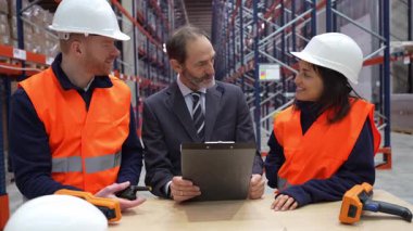 Profesyonel depo ekibi envanter lojistiğini panoyla inceliyor, iyi organize edilmiş depolama tesisinde stratejik operasyon yönetimi üzerinde çalışıyor.