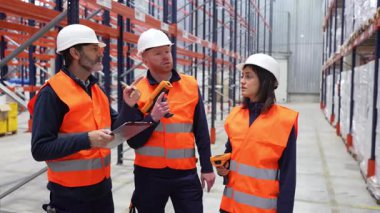 Lojistik işçileri barkod tarayıcıları ve panolar kullanarak büyük bir depoda envanter işletiyorlar.