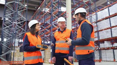 Envanter yönetimi ve dağıtım işlemlerini koordine eden profesyonel lojistik ekibi, el bilgisayarı ve işbirlikçi stratejiler kullanarak modern depo tesisi içinde