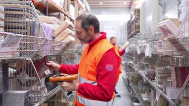 Modern lojistik dağıtım merkezindeki envanter işlerini yönetirken el bilgisayarı barkod okuyucusu kullanarak paketleri titizlikle tarayan profesyonel bir depo çalışanı.