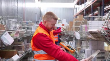 Güvenlik yeleği giyen profesyonel depo çalışanı, modern lojistik merkezinde envanteri verimli bir şekilde yönetirken barkod tarayıcısıyla paketleri tarıyor.