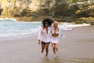 Genç, çok kültürlü bir çift güneşli sahilde neşeyle koşuyor, güneşleniyor ve yaz tatillerini birlikte kutluyorlar.