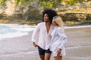 Genç, çok ırklı bir çift kumsalda gülüyor ve eğleniyor, yaz tatilinin tadını çıkarıyor.