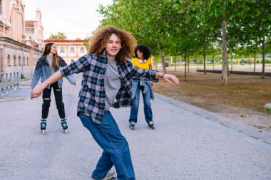 Bir grup arkadaş parkta güneşli bir öğleden sonranın tadını çıkarıyor, kaykay ve paten kayıyorlar.