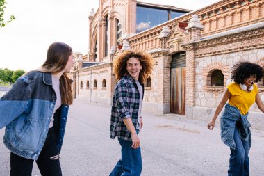 Üç genç arkadaş şehir caddesinde paten kayıyor, gülüyor ve öğleden sonra güneşinin tadını çıkarıyorlar.