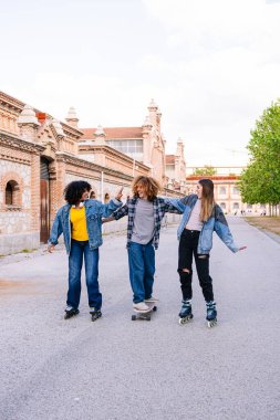 Üç arkadaş birlikte bir öğleden sonranın tadını çıkarıyor, şehir ortamında kaykay yapıyor, gençlik enerjisi ve şehir eğlencesi sergiliyor.