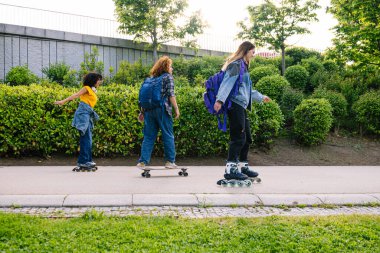 Bir grup genç kız öğrenci şehir parkında kaykay ve boş zamanlarının tadını çıkarıyorlar, aktif yaşam tarzı ve arkadaşlığı destekliyorlar.