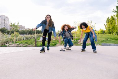 Şehir parkında kaykay ve kaykay yapan üç genç arkadaş, neşe ve özgürlüğü ifade ediyorlar.