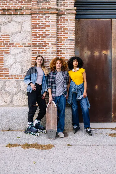 Bir grup şık genç kaykay ve patenlerle şehir duvarının yanında poz veriyorlar.