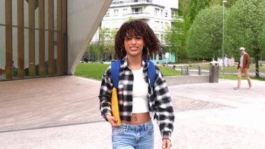 Afrikalı Amerikalı öğrenci, modern üniversite kampüsünde güvenle yürüyor akademik hırsı ve kişisel gelişimini neşeli ve kararlı bir tavırla somutlaştırıyor.