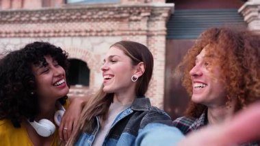 Çoklu etnik arkadaşlar hafta sonu takılırken samimi anları yakalıyorlar, kentin tuğla duvarına karşı poz veriyorlar, yavaş çekimde eğlenceli selfie çekiyorlar, gerçek neşe ve bağlantı yayıyorlar.