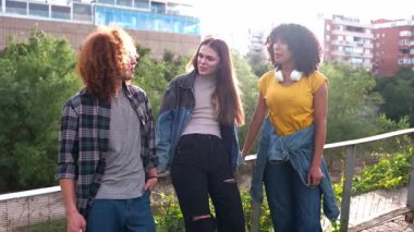 Arkadaşlar gülüyor, birlikte yürüyor, güneşli gün ışığında sakin kentsel gezintiler sırasında keyifli anları paylaşıyor, gündelik sohbetler arasında bağ kuruyor.