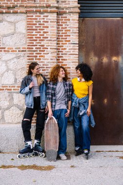 Kaykay, dahili patenler ve kulaklıklarla donatılmış üç farklı arkadaş, dokulu bir şehir zeminine karşı kahkaha ve arkadaşlığı paylaşıyorlar.