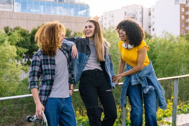 Üç arkadaş gülerek ve güneşli bir öğleden sonranın tadını çıkarırken şehir manzarasında kaykay yaparken, gençlik ve arkadaşlığı kucaklıyor.