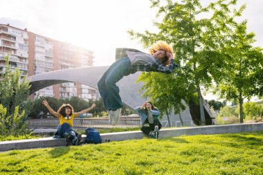 Arkadaşların parkta güneşli bir günün tadını çıkarıyorlar. Gündelik giysiler giyerken ters takla atıyorlar. Patenler ve sırt çantasıyla.