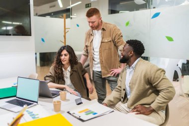 İş ekibi birlikte çalışıyor, dizüstü bilgisayardaki verileri analiz ediyor ve proje stratejisini parlak, modern bir çalışma alanında tartışıyor.