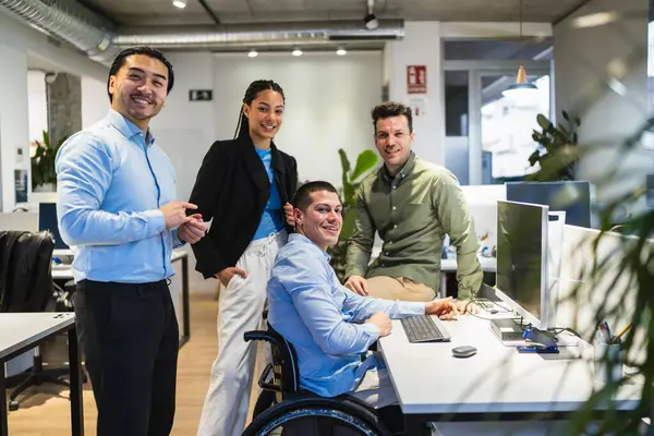 Bir grup genç profesyonel, tekerlekli sandalye kullanan engelli bir meslektaşla birlikte modern bir çalışma ofisinde işbirliği yapıyor.