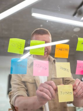 Kafkasyalı yönetici cam duvara renkli yapışkan notlar yapıştırıyor, işi için yeni bir strateji geliştiriyor.