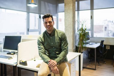 Masasında oturan gülümseyen bir iş adamının portresi. Ortak, modern bir ofis alanı, özgüven ve başarının simgesi.