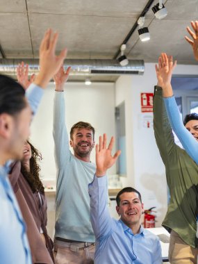 Hevesli genç profesyoneller ellerini kaldırarak modern bir ofis alanı içinde aktif bir işbirliği toplantısına katılıyorlar.