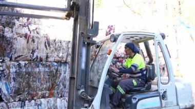 Forklift operatörü yavaş çekimde yakalanan karton balyayı geri dönüşüm merkezinde bir yığın üzerine dikkatlice yerleştiriyor.